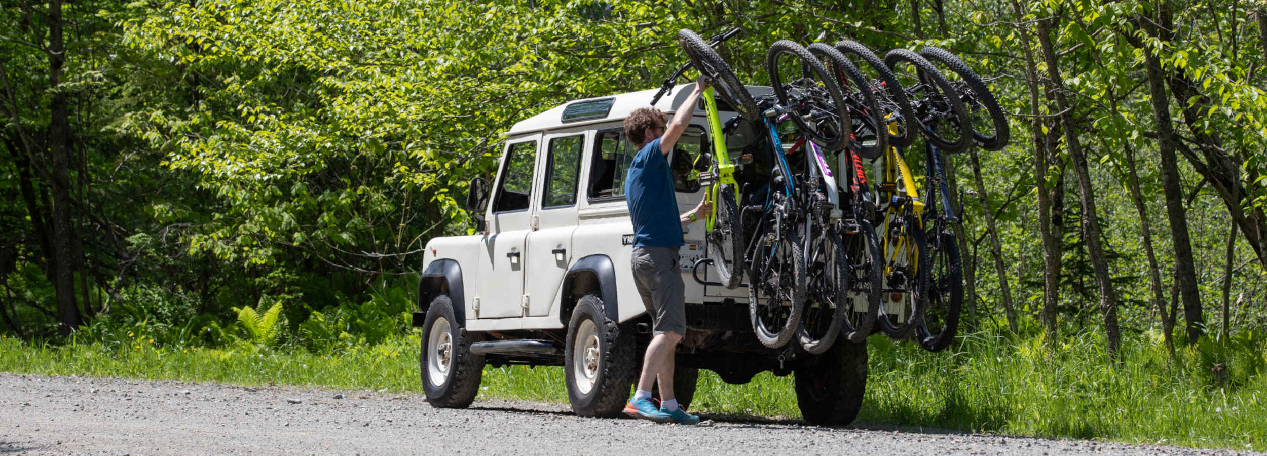 Un homme attache un vélos sur un rack Panache installé sur un LandRover.