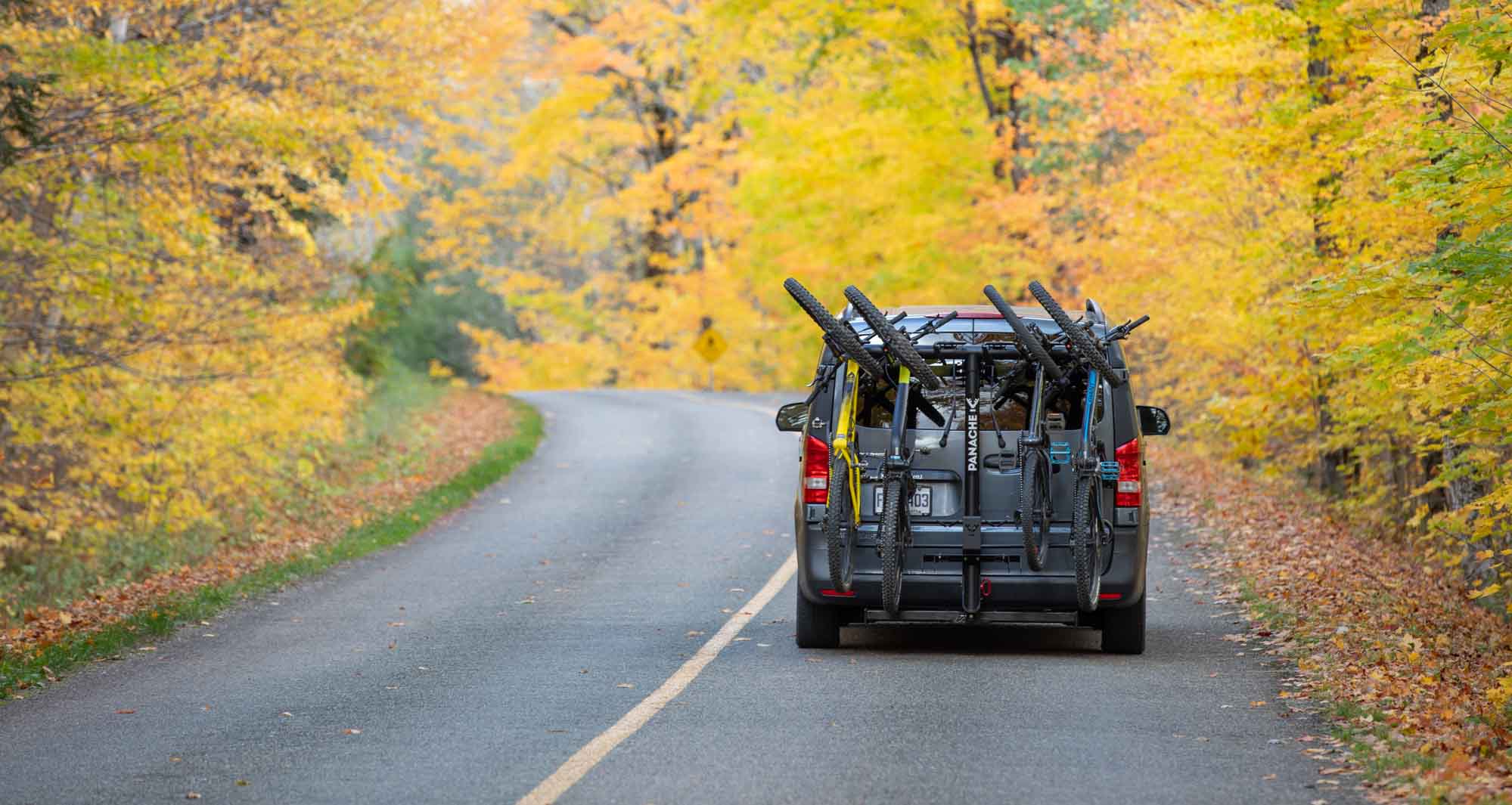 Mini van on a small country road with nice Fall colors equiped with a Panache Rack T4 bike rack carrying 4 bikes.