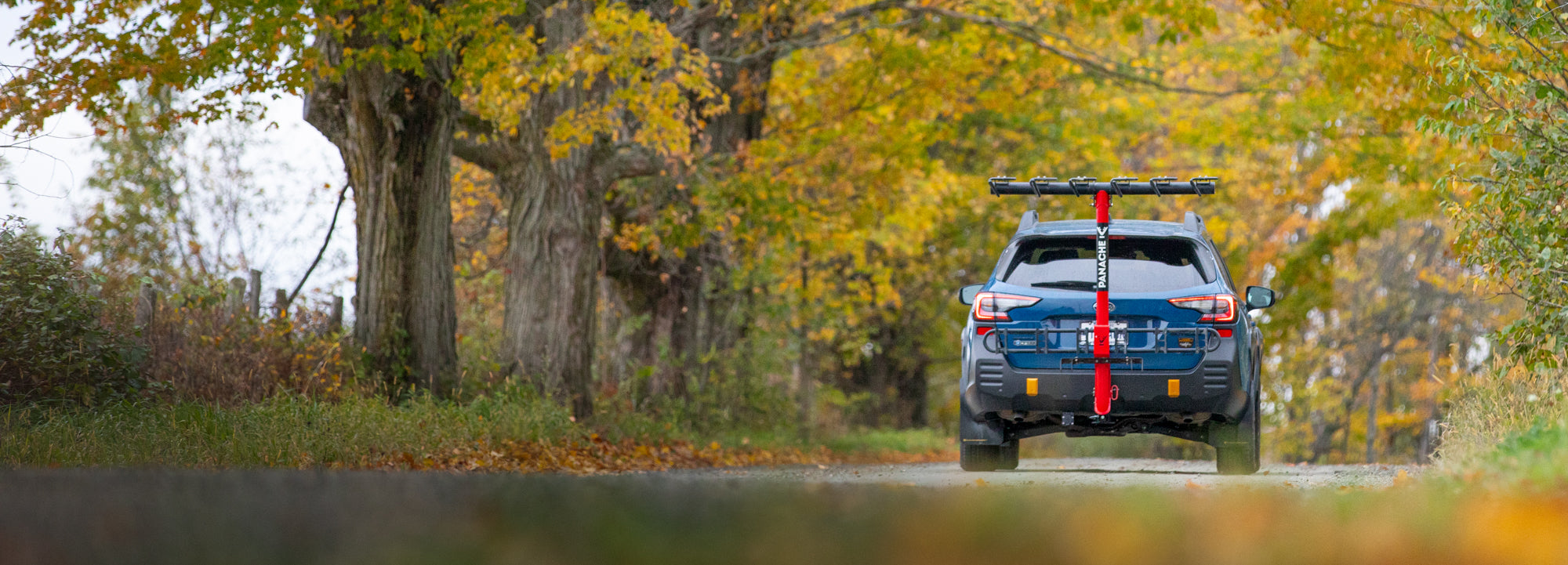 Horizontal picture of a Subaru equipped with a T6 Panache Rack bike rack coming down a nice dirt road in fall